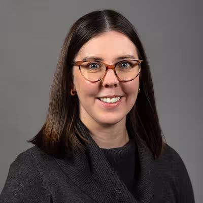 Nyssa Knarvik smiles in glasses and a dark gray sweater in front of a gray backdrop