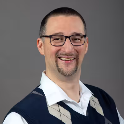 Dr. Timothy "Julio" McLaughlin portrait smiling with glasses and sweater vest