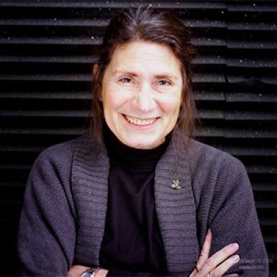 Rosemary Armao smiles in a dark turtleneck and brown cardigan against a dark brink backdrop.