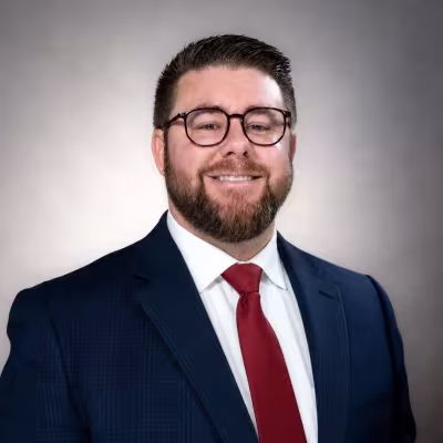Smiling portrait of Michael Colello in a dark suit with a white shirt and red tie. 