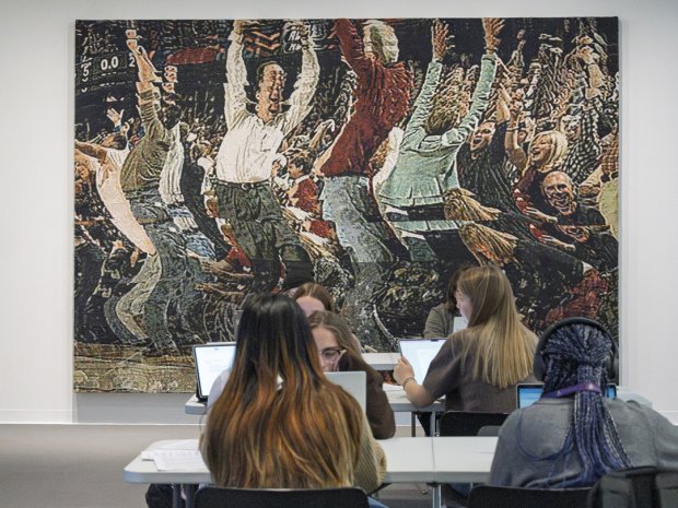 Students working on laptops in front of tapestry work
