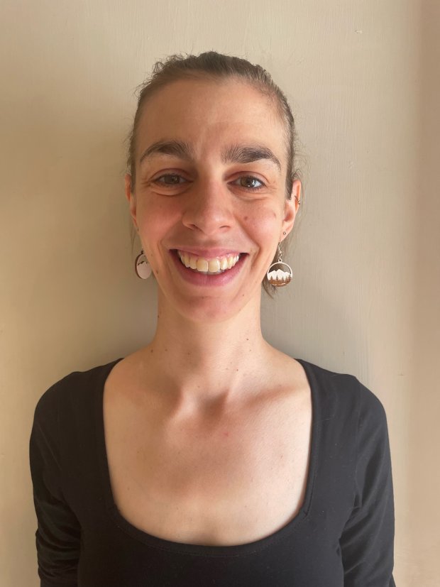 A young woman wearing a black top smiles for a portrait against a beige wall. 