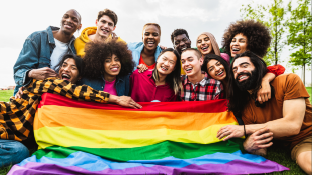 A group of students gathered around a rainbow pride flag and smiling
