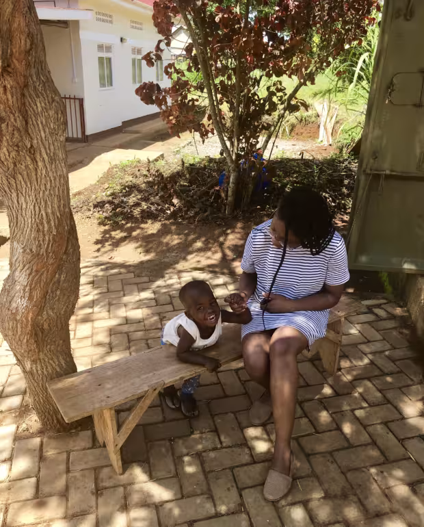 Jenee sitting on a bench in Uganda with a small child.