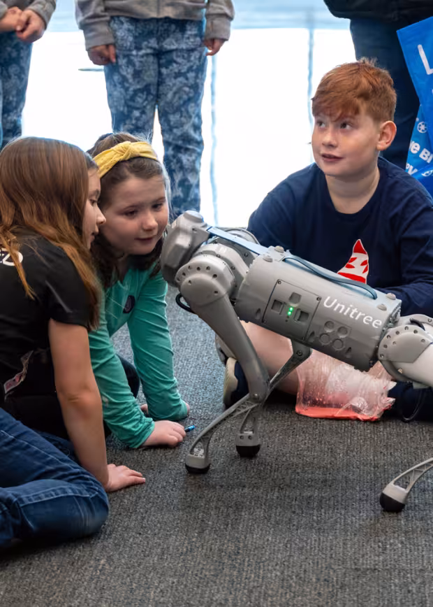 Three children interacting with a robot dog at UAlbany STEM and Nanotechnology Family Day.