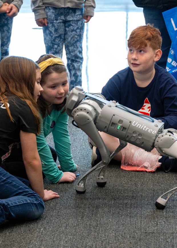 Three children interacting with a robot dog at UAlbany STEM and Nanotechnology Family Day.