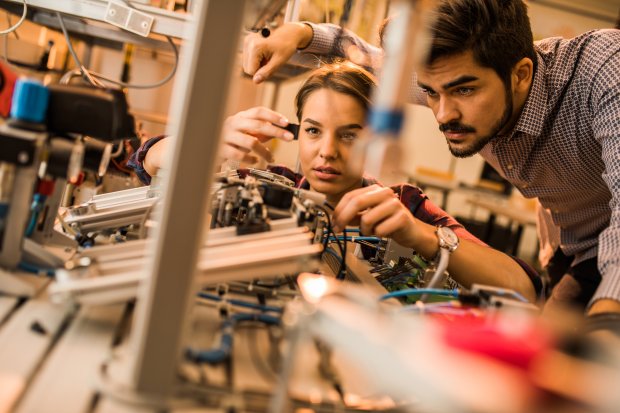 Two engineering students working on electrical component of a machine in laboratory