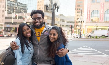 Three students stand on an Albany street, smiling at the camera.