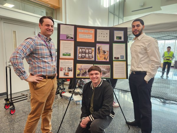 CEHC Lecturer Frank Peris stands with students Jay Parker and Hadley Santos in front of a poster board presentation at ETEC.