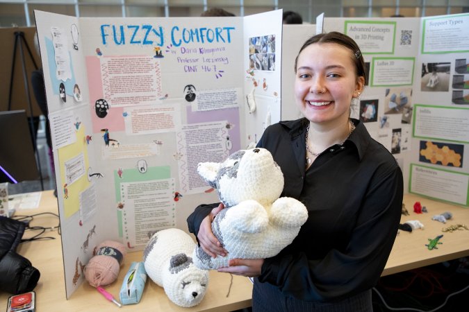 Daria Kolmogorova holds a stuffed animal in front of her poster project at the CEHC Fall 2023 Showcase.