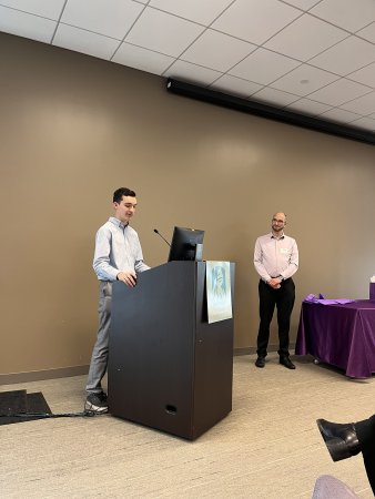 Political science student Trevor Pettit stands at the podium to give remarks about his professor Brian Greenhill, standing to the right of him..