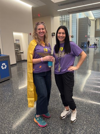 Jen Goodall stands with a super hero cape on next to Erin Couture at the ETEC atrium.