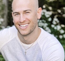 Andrew Petsche smiling outdoors with gray and white sweater