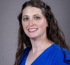 individual in blue top with long brown hair, gray portrait background