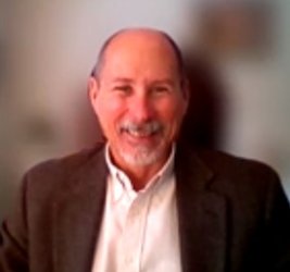 Dr. Michael V. Ellis smiling in white dress shirt and brown jacket with blurred background
