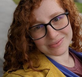 Catarina Alves smiling outdoors with red hair, glasses and yellow jacket