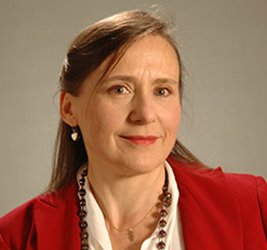 Karin Reinhold wears a red blazer, a red beaded necklace, a silver chain and silver earrings, against a neutral background.