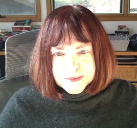 Mary Valentis sits at her desk. She wears a gray sweater and her auburn hair is cut shoulder-length with bangs.