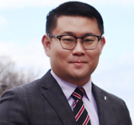 Pete Kwon stands outside in a black suit and glasses against a cloudy sky.