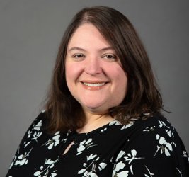 Johanna Cole smiles wearing a black and white floral shirt against a gray backdrop
