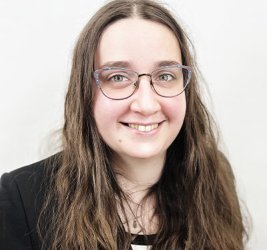 Cécilia Légaré wears glasses and smiles in a black blazer and white shirt in front of a plain backdrop.