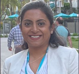 Kahini Sarkar stands outside smiling in a white blouse, white blazer and white bouse.