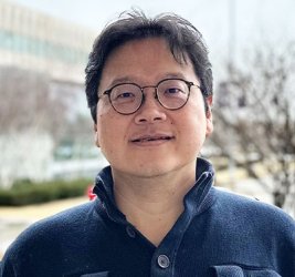 Tse-Chuan Yang stands on UAlbany campus wearing glasses and a navy pullover.