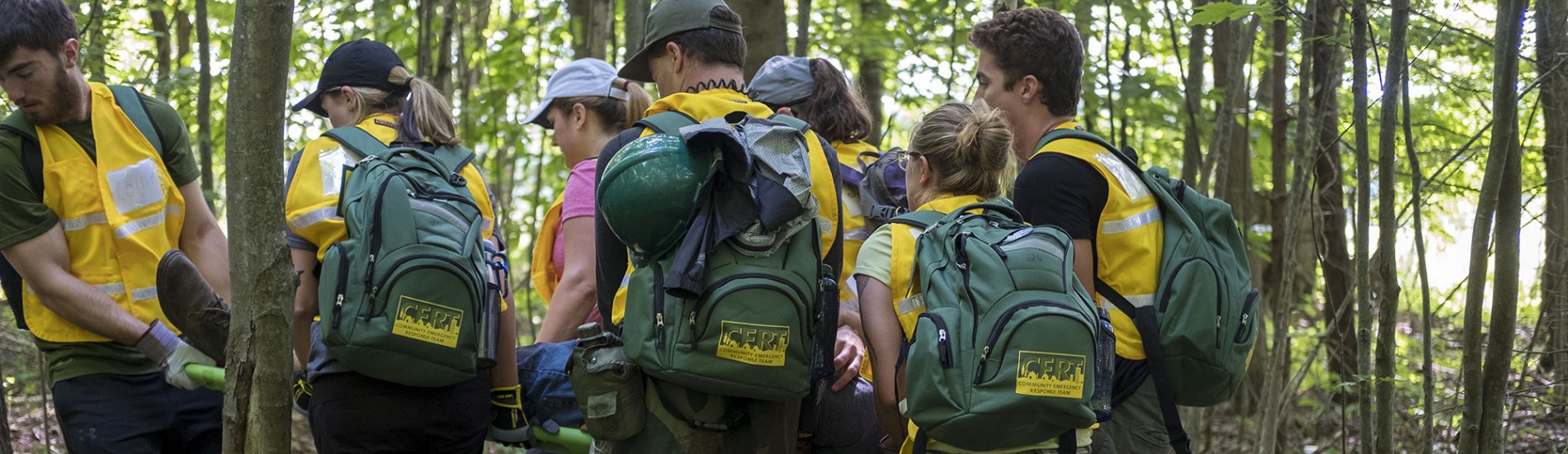 A group of students wearing backpacks doing field training in the woods.