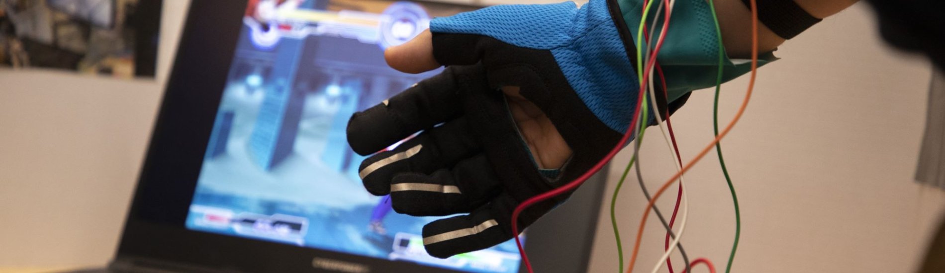 Student wearing a controller glove wired up to a laptop.