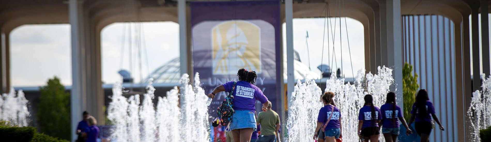Students walking through the entrance fountain wearing Proud Transfer shirts.