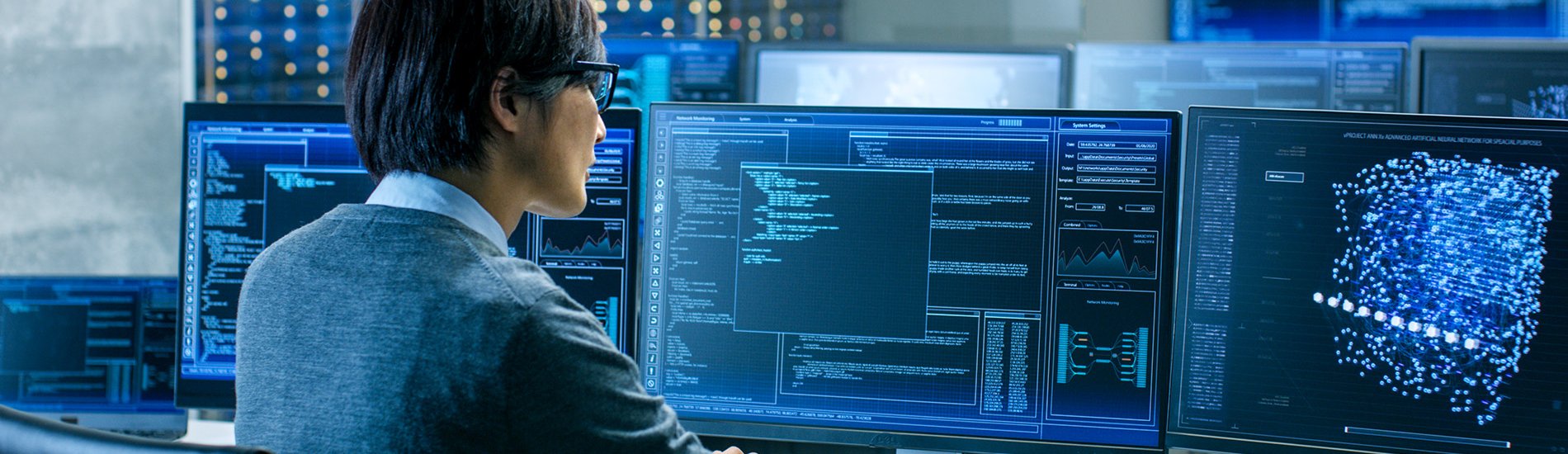 A researcher reviewing data on multiple computer monitors.