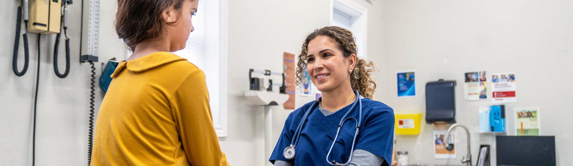A nurse working with a young patient in a medical exam room.