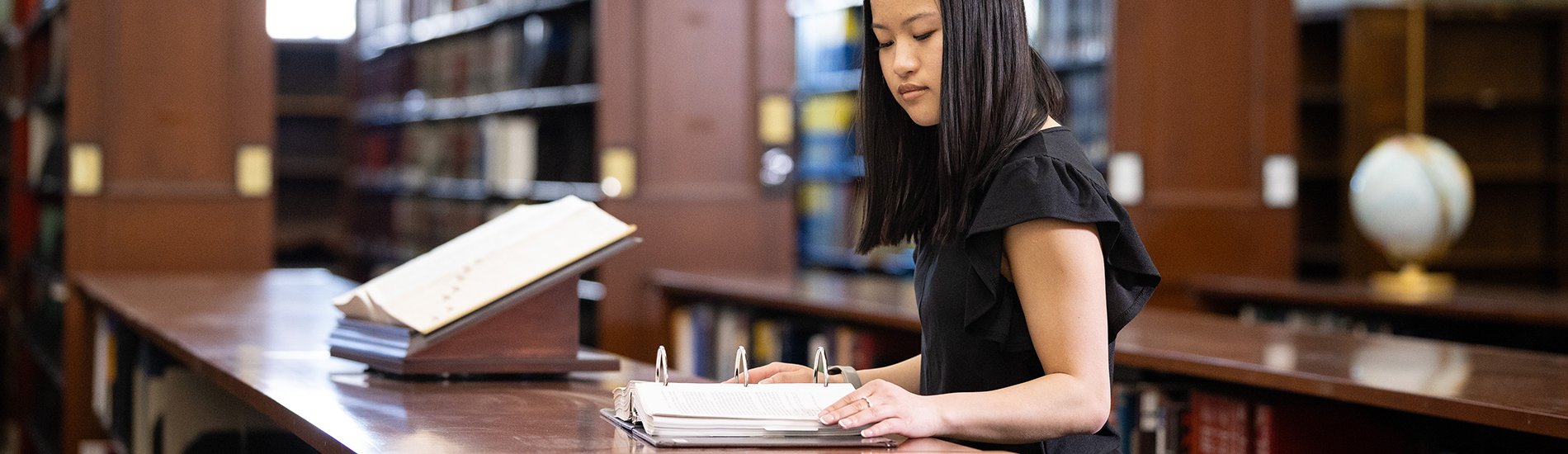 A student reading a reference book in the UAlbany Dewey Library.