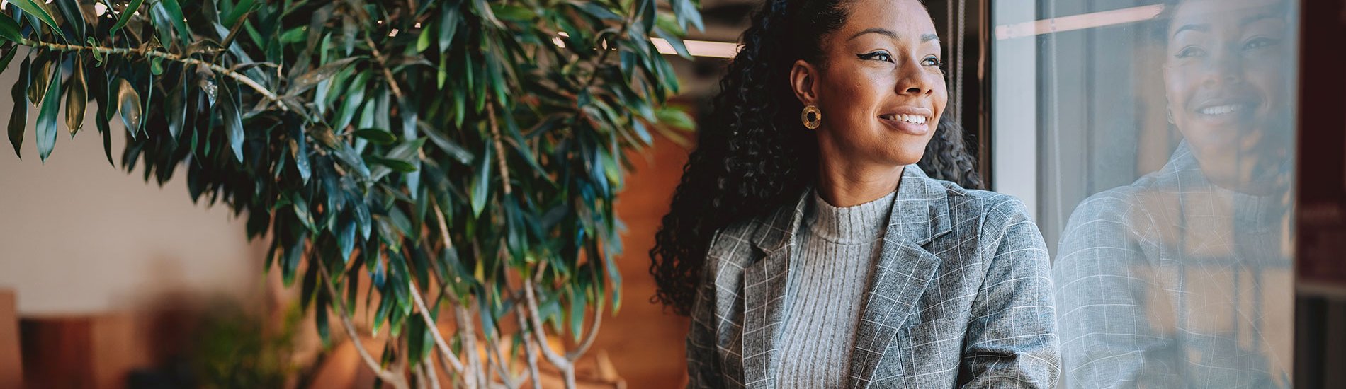 A smiling professional in communications or marketing sitting by a window holding a laptop.