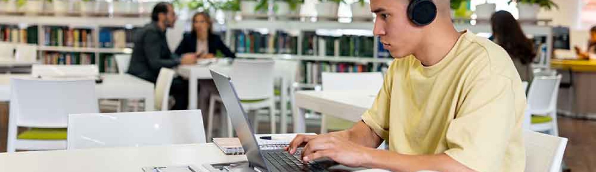 A student on his laptop in the library attends online classes.