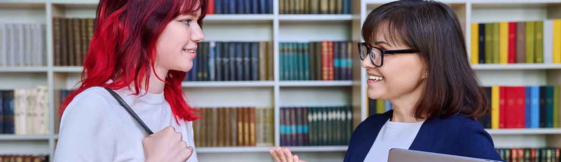 An academic advisor talks to a student in the school library.