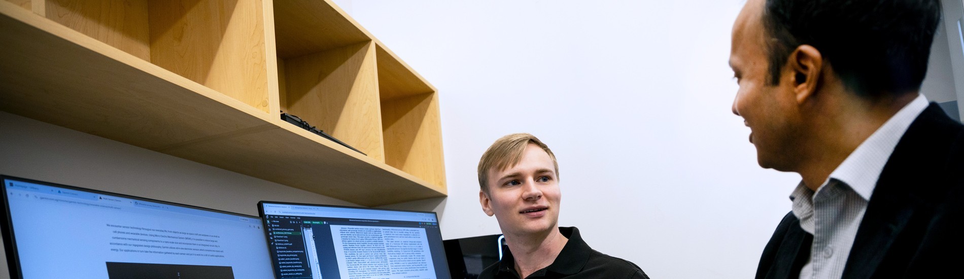 A student and professor reviewing data on two computer monitors.
