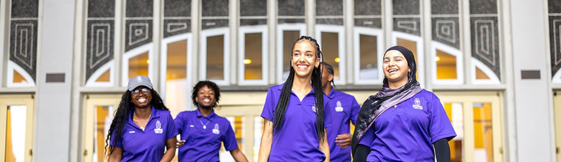 A group of orientation leaders wearing UAlbany polo shirts walking out of campus center. 