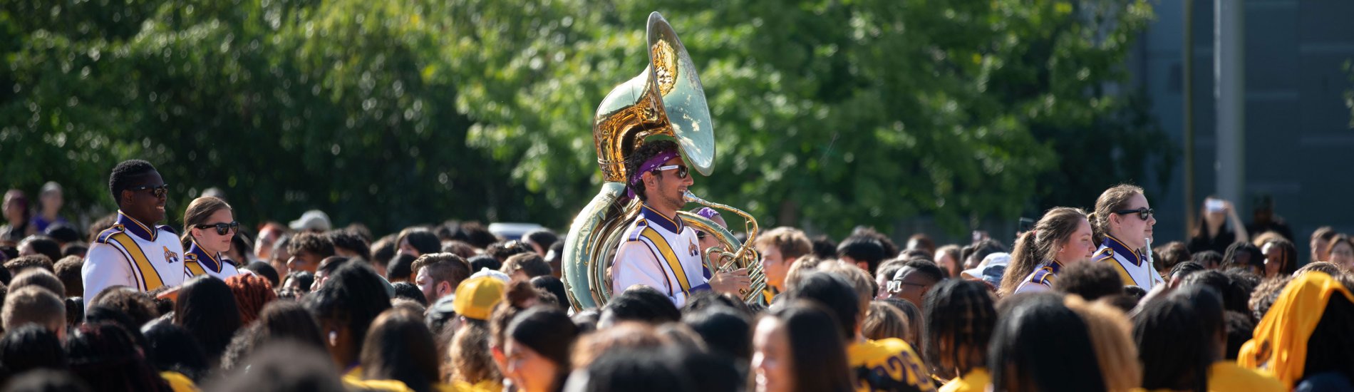 A tuba player in the UAlbany Marching Band walks through a crowd of students in yellow t-shirts.