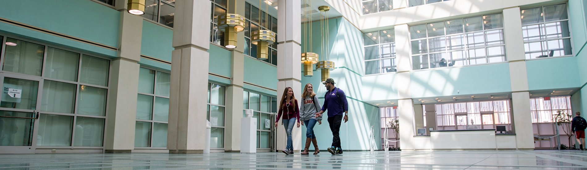 A group of three students walking through the UAlbany Science Library lobby.