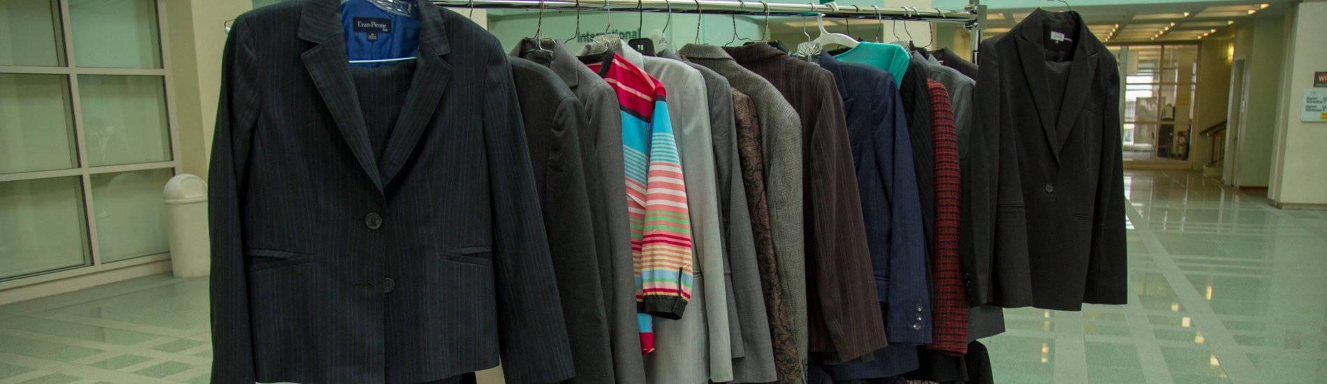 A clothing rack loaded with suits and other professional clothing is positioned inside an atrium.