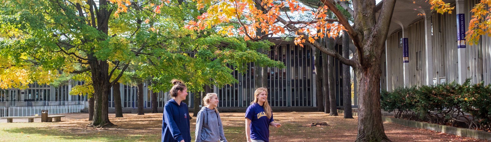 Three students walk across a residential quad surrounded by fall foliage