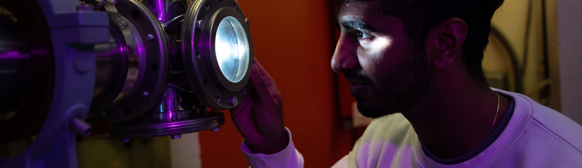 A student's face is lit up as he looks into a piece of lighted instrumentation.