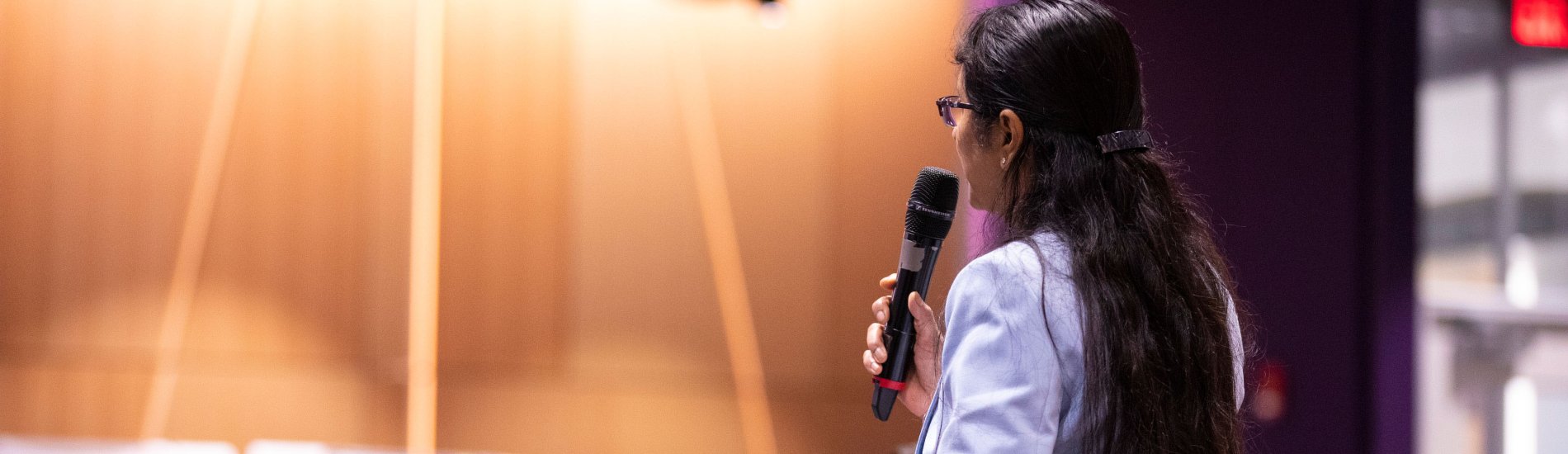 A woman stands among a seated crowd at a UAlbany AI Plus event and speaks into a microphone to ask a question.