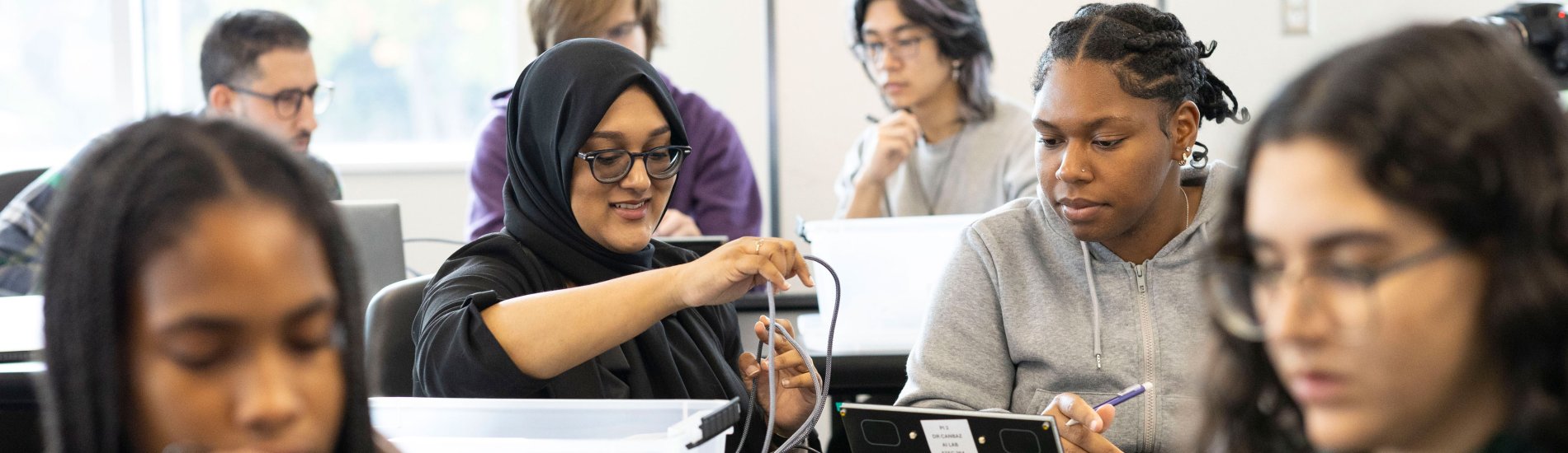 Two students sit inside a full classroom and work together to build an electronic device during an AI-focused class.