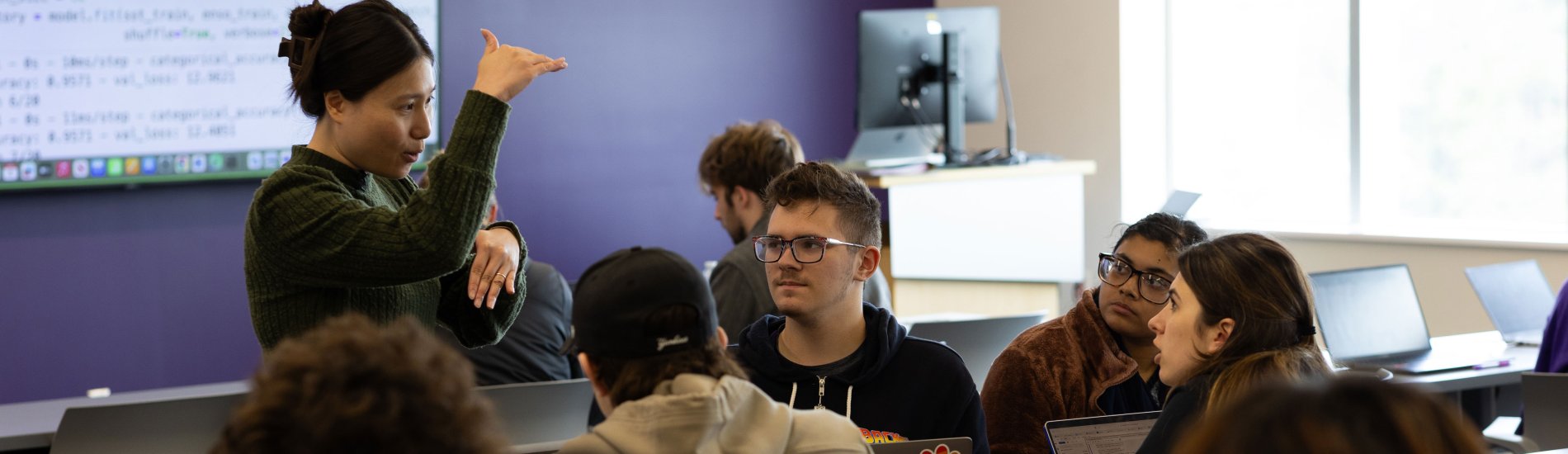 A UAlbany professor gestures as she speaks to a group of students working in a full classroom.
