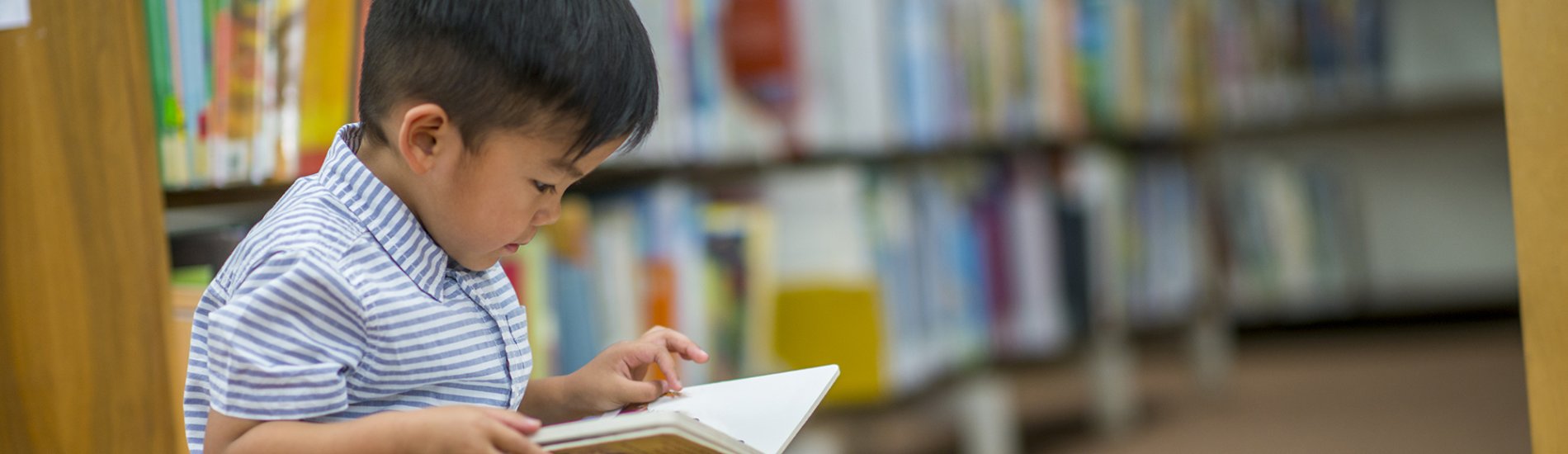 Young child reading a book in a library.