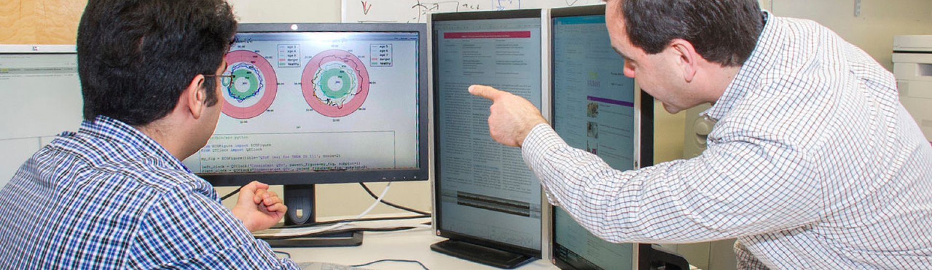 Two UAlbany researchers reviewing data on multiple computer screens.