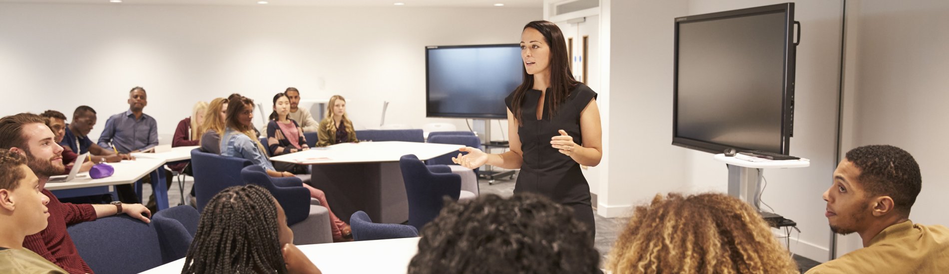 Female teacher addressing university students in a classroom. 