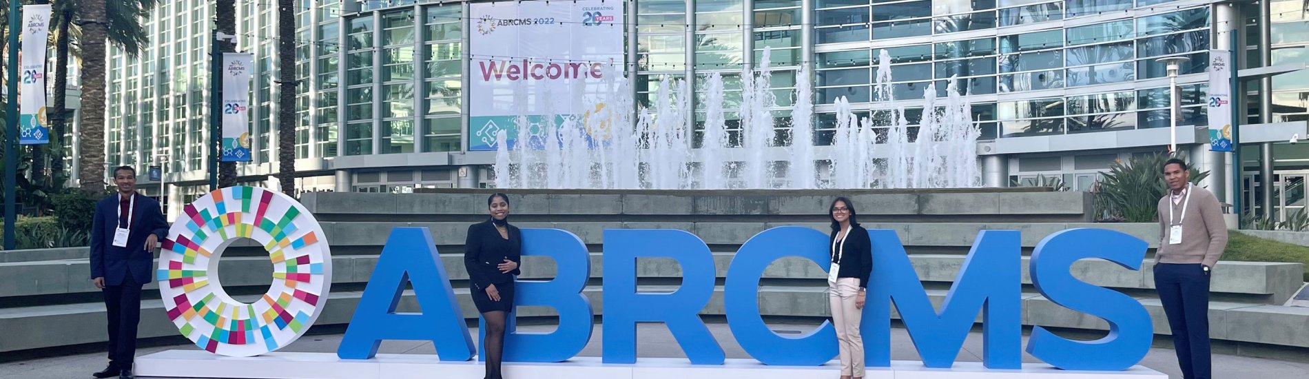 Four students in business casual clothing pose with the Annual Biomedical Conference for Minority Students (ABRCMS) logo